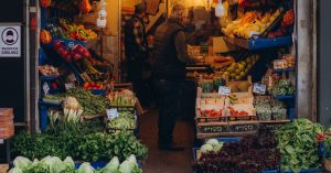 Vibrant street market stall displaying fresh vegetables and fruits with people shopping.