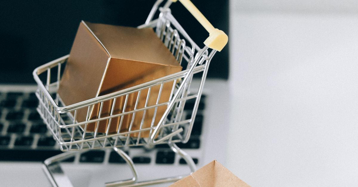 A miniature shopping cart with a parcel on a laptop symbolizes online shopping and e-commerce.